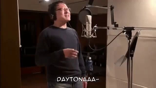 a man is singing into a microphone in a recording studio and the words daytonaaa are above him .