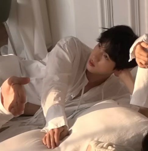 seokjin in slightly skimpy white fit leaning against a white bedding