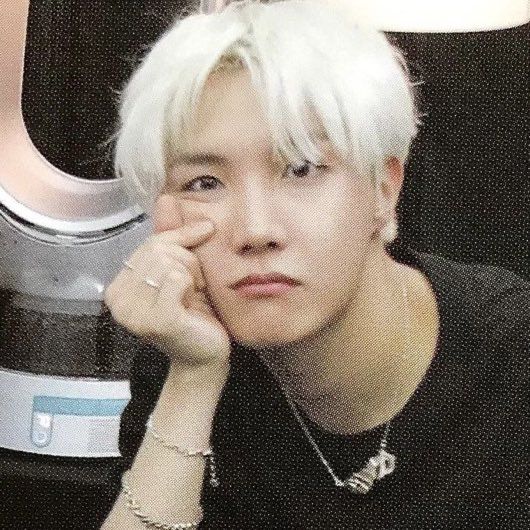 hoseok with white blonde hair and black tee. he’s squishing his cheek with the small finger hearts 