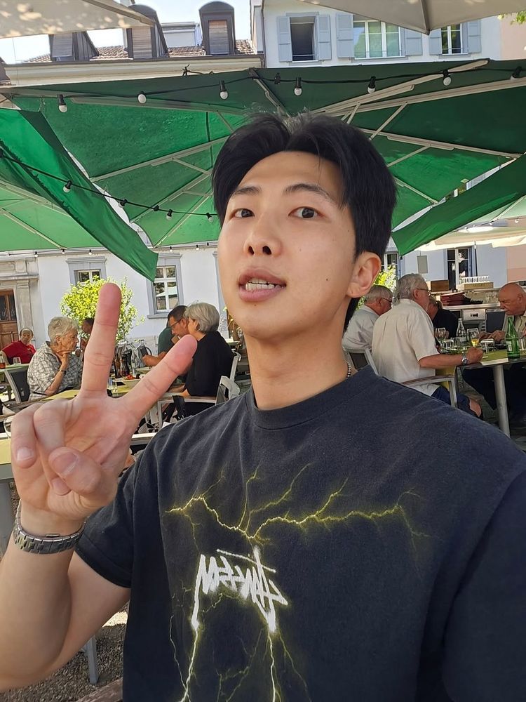 namjoon selfie at an outdoor seating at a restaurant. he’s holding up a v sign, his chest is broad, his adam’s apple is sexy as hell
