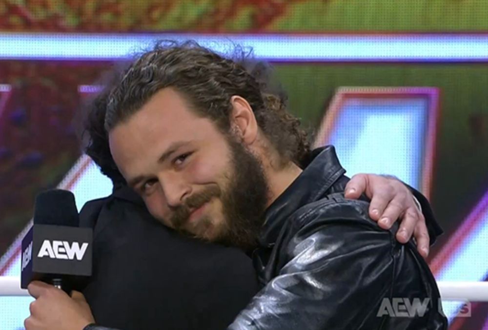 Jack Perry giving his boss a hug and smiling innocently smiling at the camera  