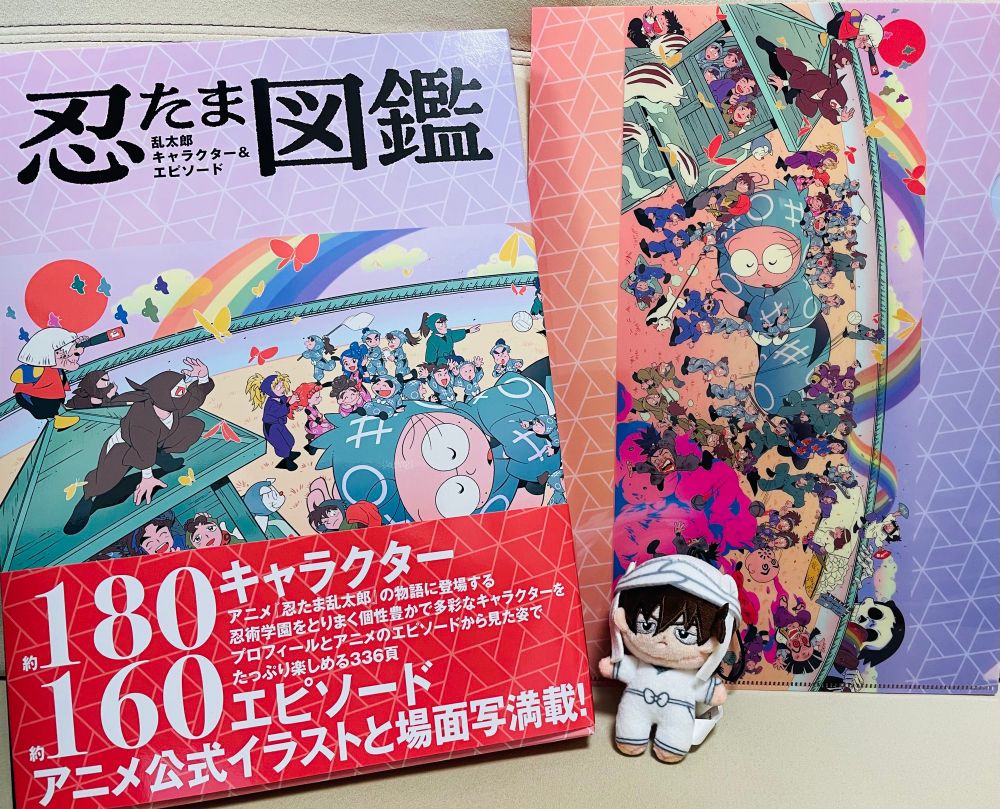 厚さが2.5センチくらいある忍たま図鑑と、特典のクリアファイル。手前にほわぬい天鬼がいる。