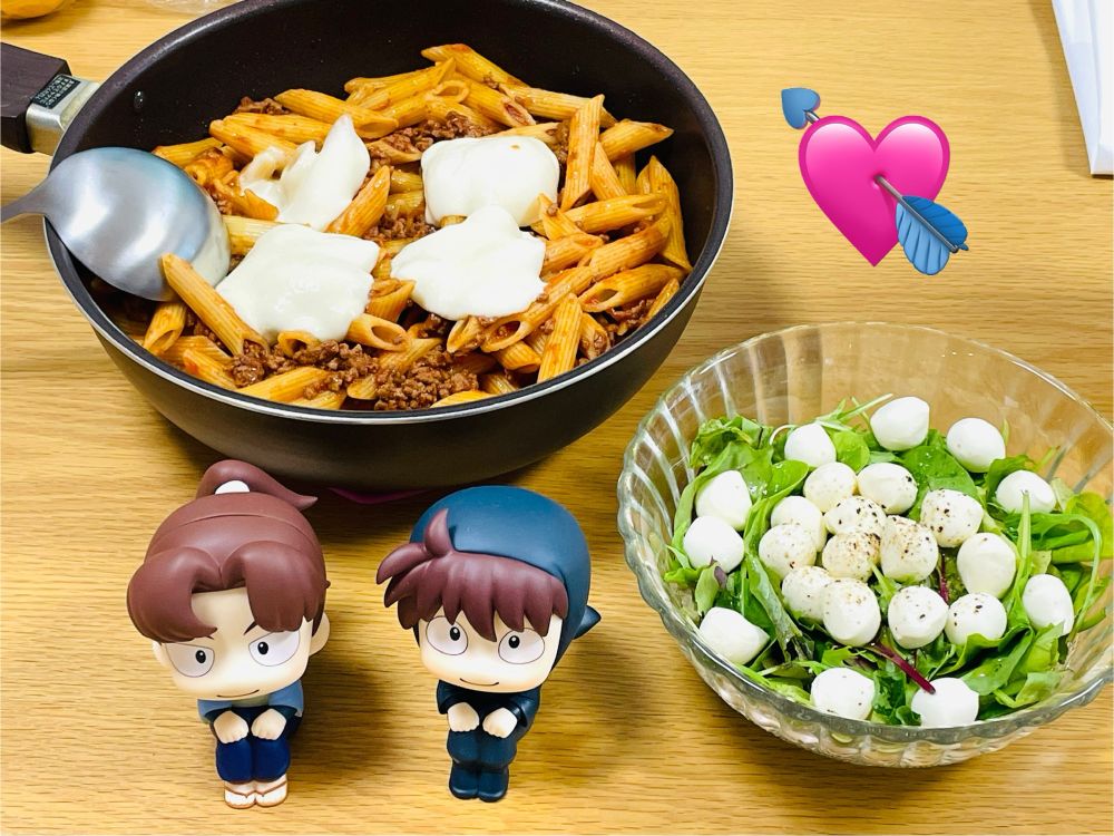 フライパンに利吉の的当てモッツァレラのミートソース、その右にモッツァレラチーズたっぷりのサラダ。
手前にるかっぷの利吉さんと土井先生がいる。