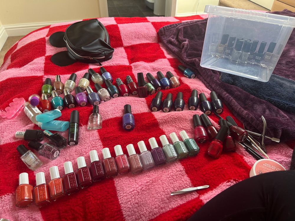 Pink and red checkerboard duvet with circa 70 nail polishes laid out. Brands OPI, Essie, China Glaze and Holo Taco. Also assorted nail tools.