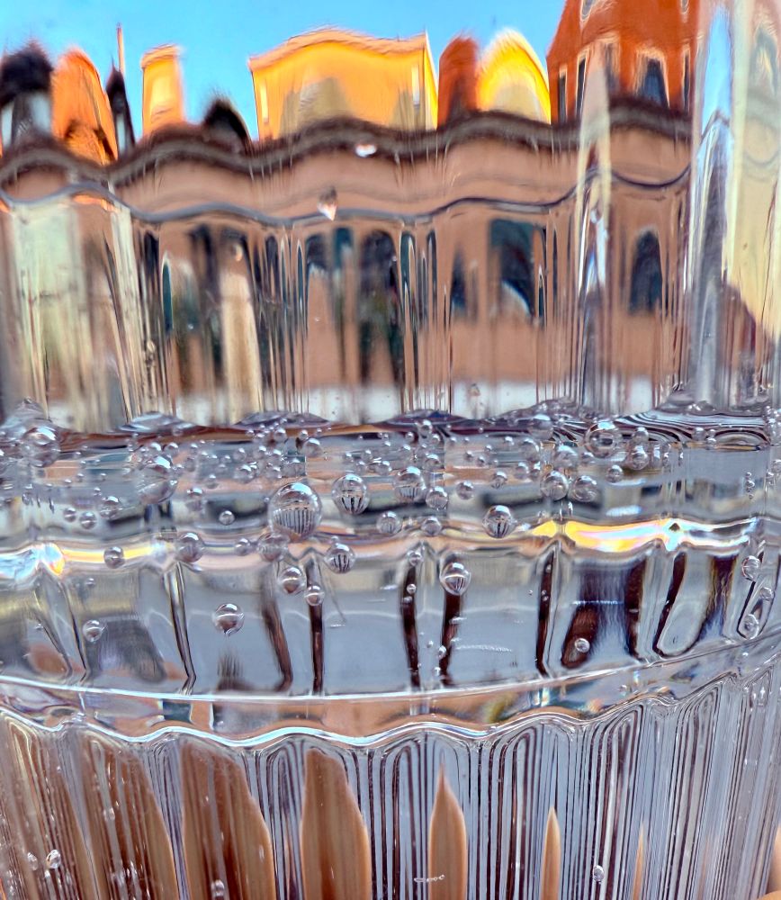 Photo taken through a drinking glass showing distorted image of buildings and mineral water bubbles.
