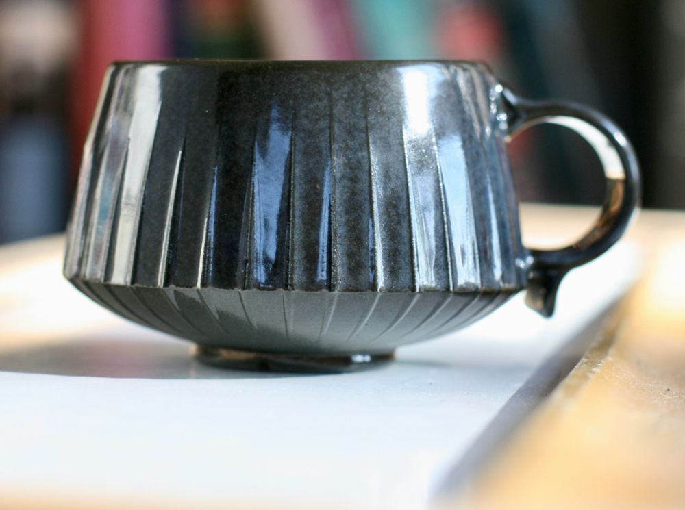 Black porcelain mug glazed in dark blue. The flaw in this piece is the clear liner glaze application on the inside. Too thick, crawled badly. Still usable because porcelain but very unsightly