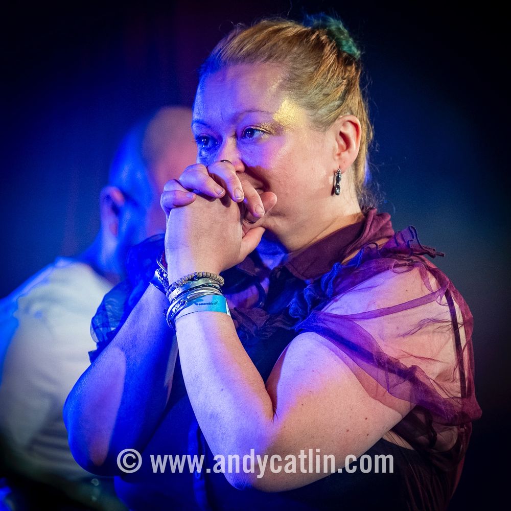 A singer onstage during a concert with the hands held together in front of to their face