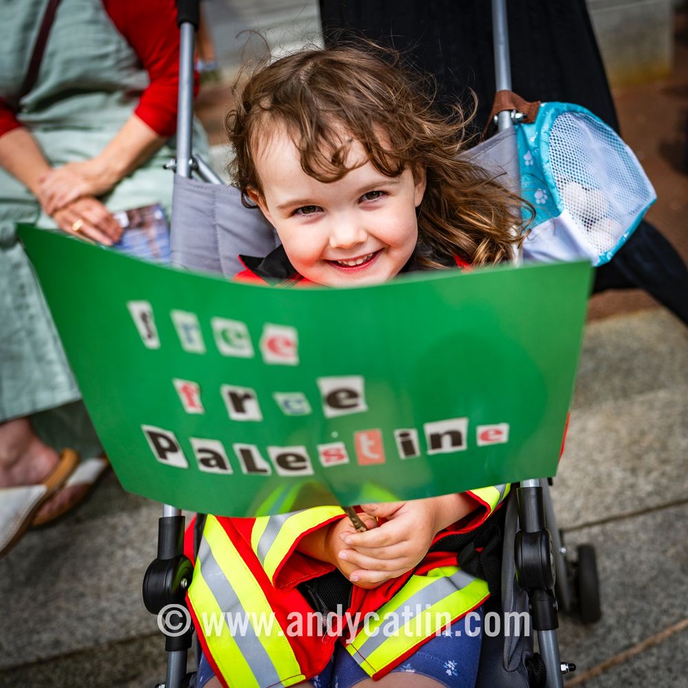 A smiling child holds a placard reading "Free Free Palestine"