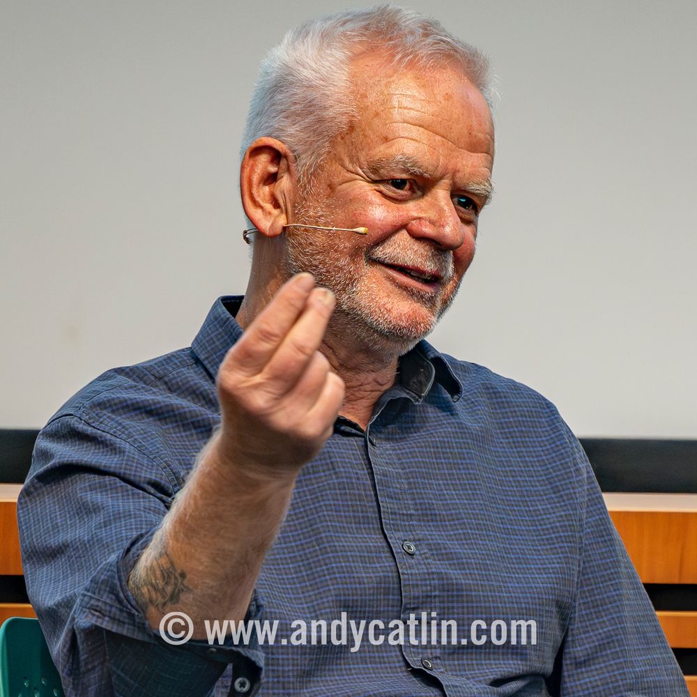 An artist speaking at a lecture with their right hand raised up