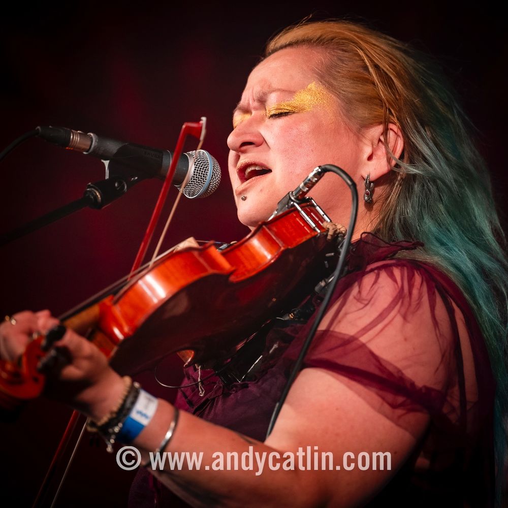 A fiddle player onstage during a concert singing into a microphone