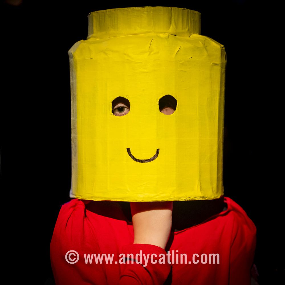 An actor wearing a yellow mask Lego helmet which has a smile drawn on the front