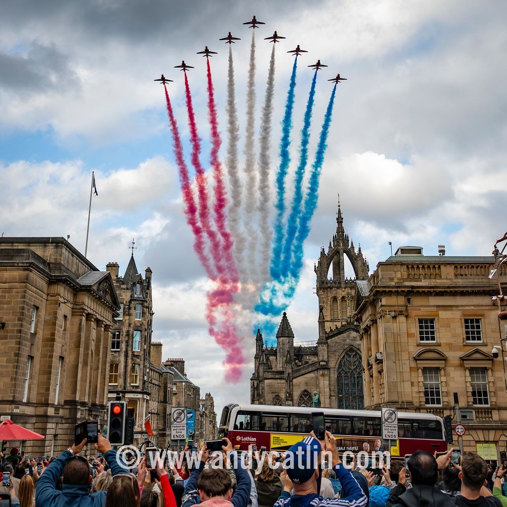 Nine military aircraft with multicoloured smoke trails fly in a arrow formation over Edinburgh city centre.
