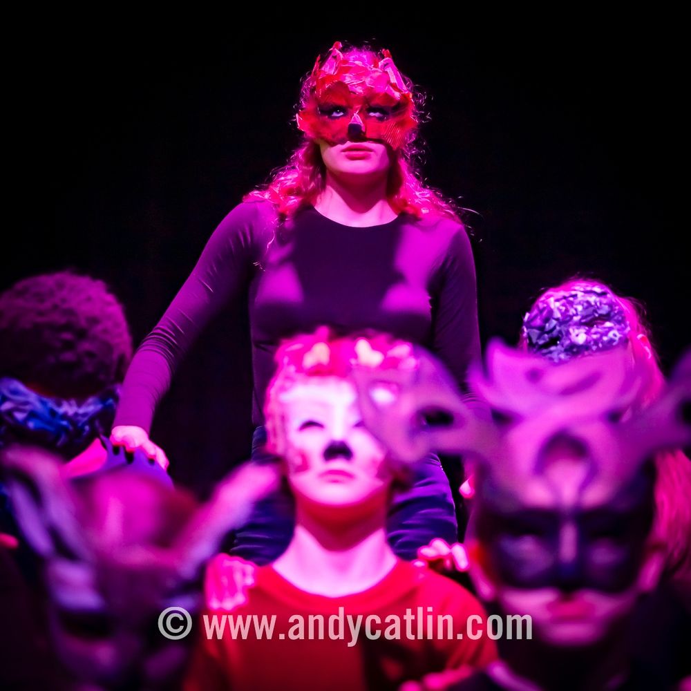 A group of young actors onstage during a performance who are all wearing masks over their faces
