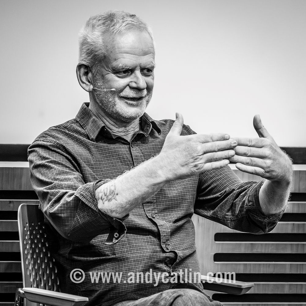 An artist speaking at a lecture with their hands raised in front of them
