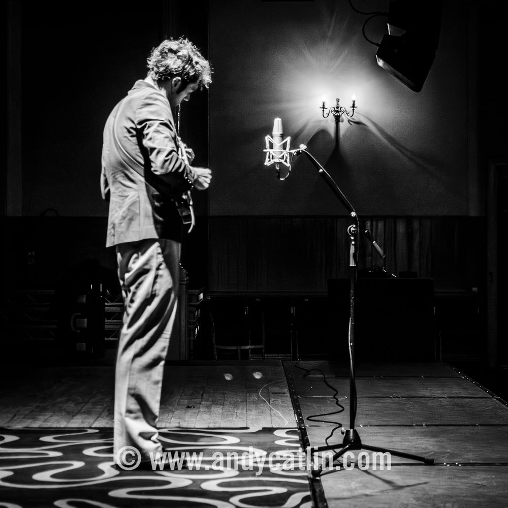 A black and white photo of a mandolin player onstage during a concert