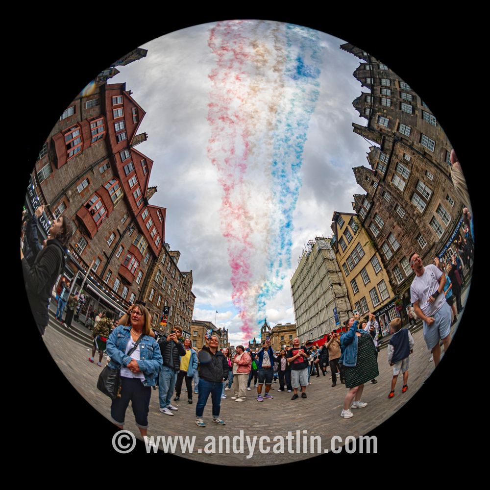 A fisheye image of Edinburgh city centre with multicoloured smoke trails in the sky