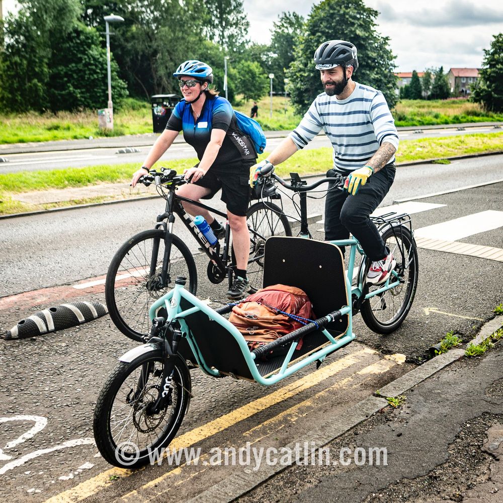 Two smiling cyclists riding next to each other in a bike lane next to a road