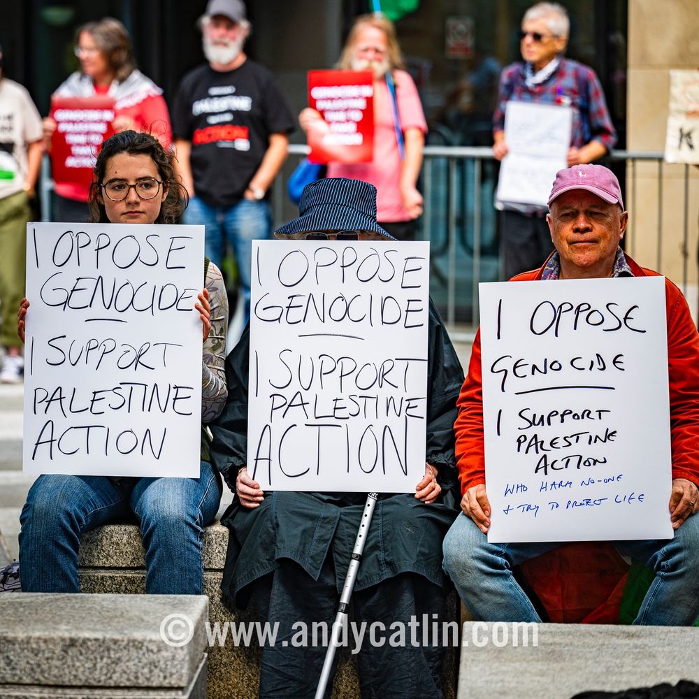 Three protesters holding signs that read "I Oppose Genocide: Support Palestine Action"