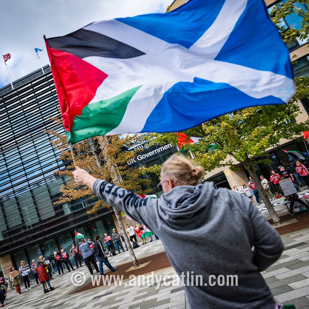 A protester at the Lift the Ban demonstration waving a combined Scotland and Palestine flag in front of a UK Government building 