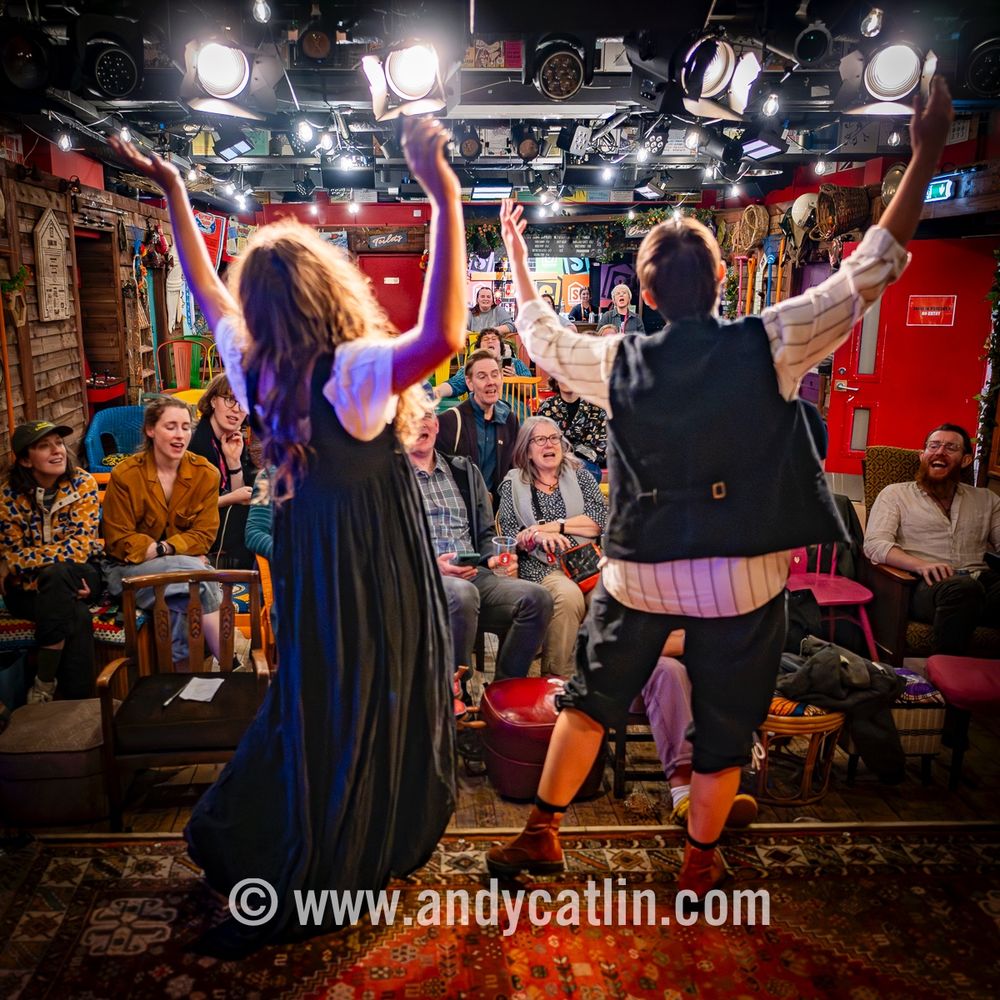 Two actors onstage with the arms raised singing at the audience 