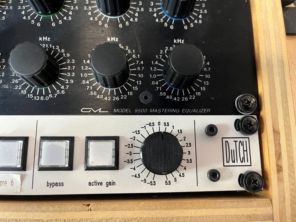 A close-up of the right side of a GML Model 9500 Mastering Equalizer, showing several rotary frequency knobs labeled in kilohertz and a white control panel below with buttons labeled “bypass” and “active gain.” A large black gain knob is marked from -5.5 to +5.5 dB. The logo “DuTCH” is printed in a hand-drawn style on the bottom right. The unit is mounted in a wooden rack with visible black screws.