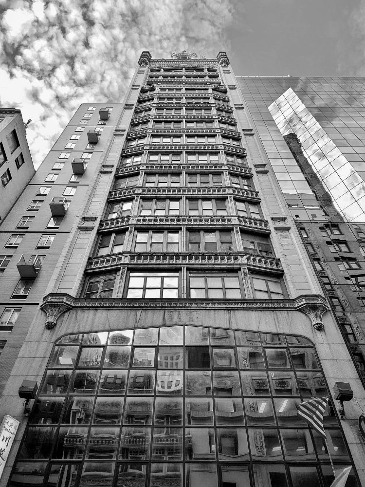 A black-and-white photo of a tall, ornate building with reflective glass windows in Midtown Manhattan, Manhattan, New York.