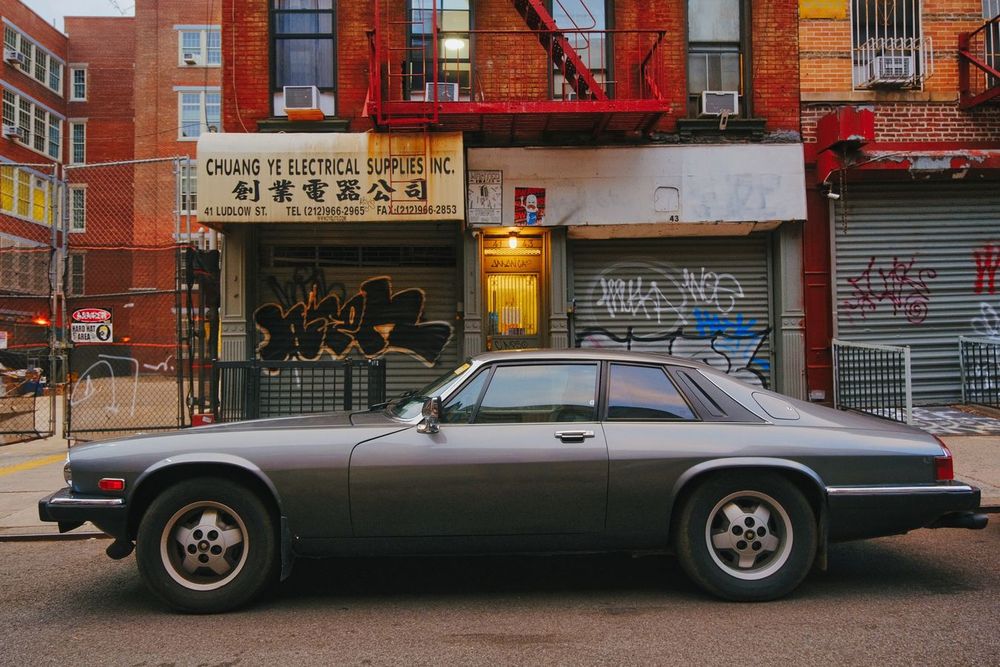 A vintage car is parked in front of a graffiti-covered storefront under a fire escape in the Lower East Side, Manhattan, New York.