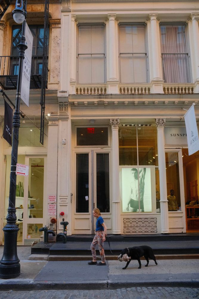 A person walks a black dog past a storefront in SoHo, Manhattan, New York.