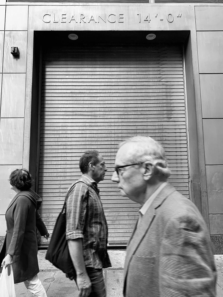 Three people walk past a garage door with a clearance sign in Midtown Manhattan, Manhattan, New York.
