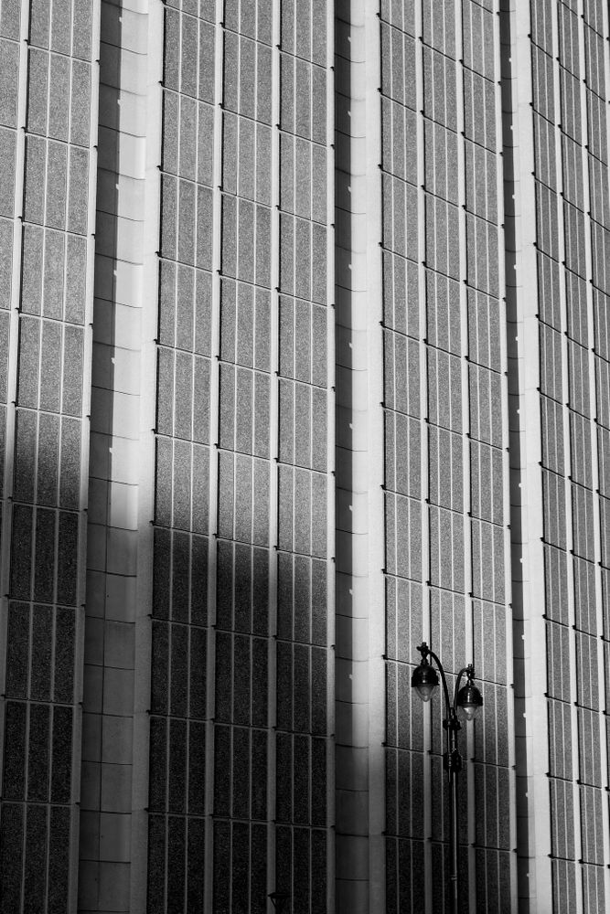 The image shows the facade of a building with tall windows casting shadows and a streetlamp in the foreground in Midtown Manhattan, Manhattan, New York.