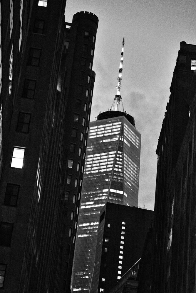 A view of a modern skyscraper with a spire framed by surrounding buildings in the Financial District, Manhattan, New York.