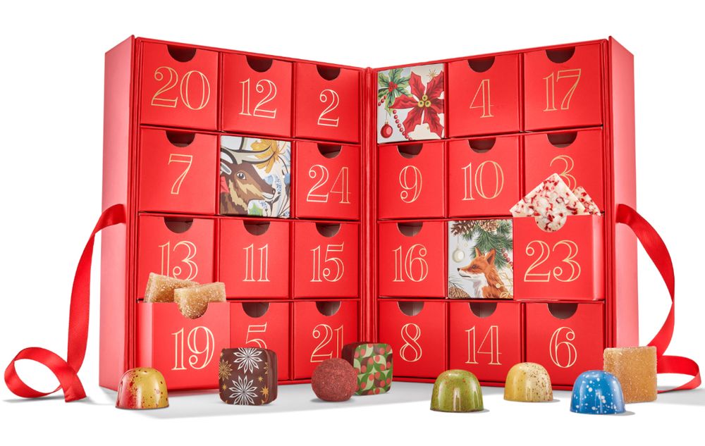An advent calendar with little drawers surrounded by colorful bonbon chocolates and holiday designs