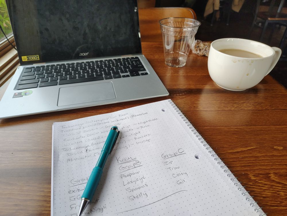 Chromebook, open notebook with names and magic occupations, cup of coffee