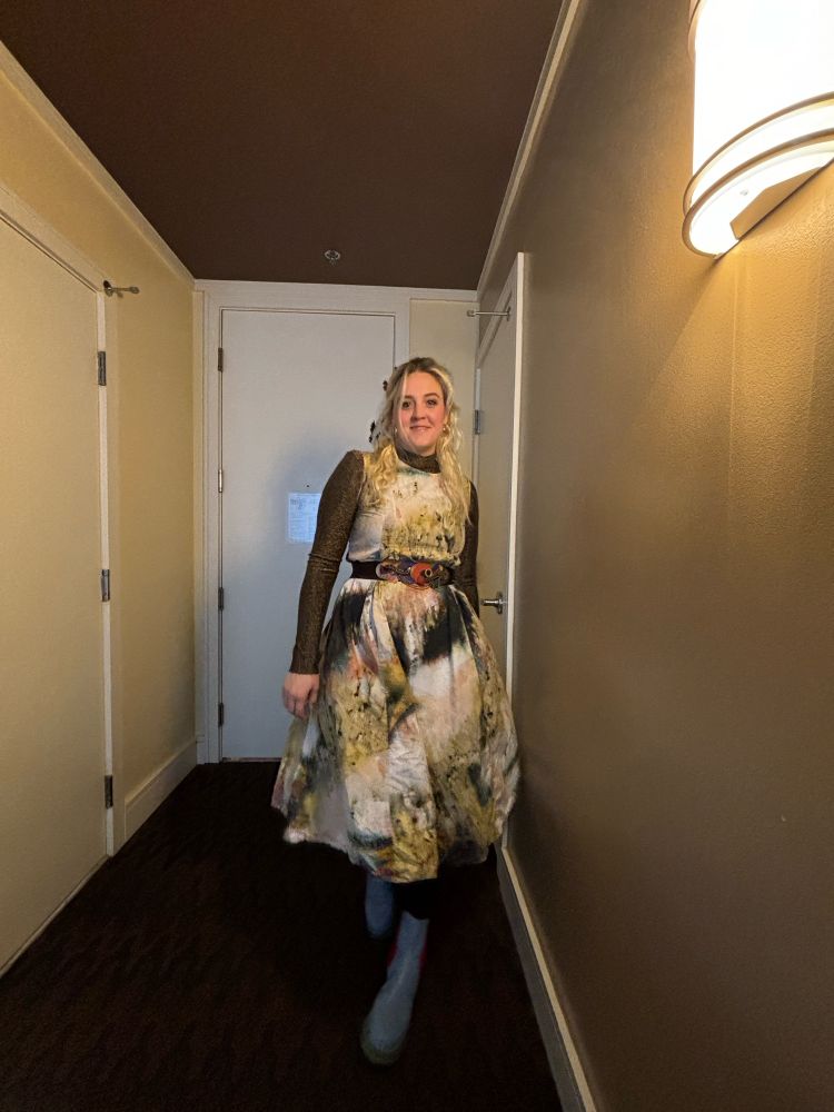 white woman with bleached hair and a long dress with a sparkly long sleeve shirt underneath, a belt, and light blue boots