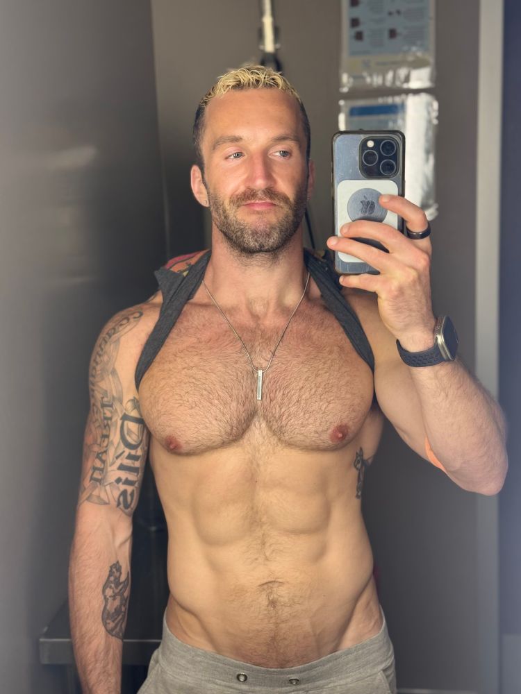 Shirtless gay guy taking a picture in a bathroom mirror well technically his shirt is just pulled behind his neck but you get the drift 
