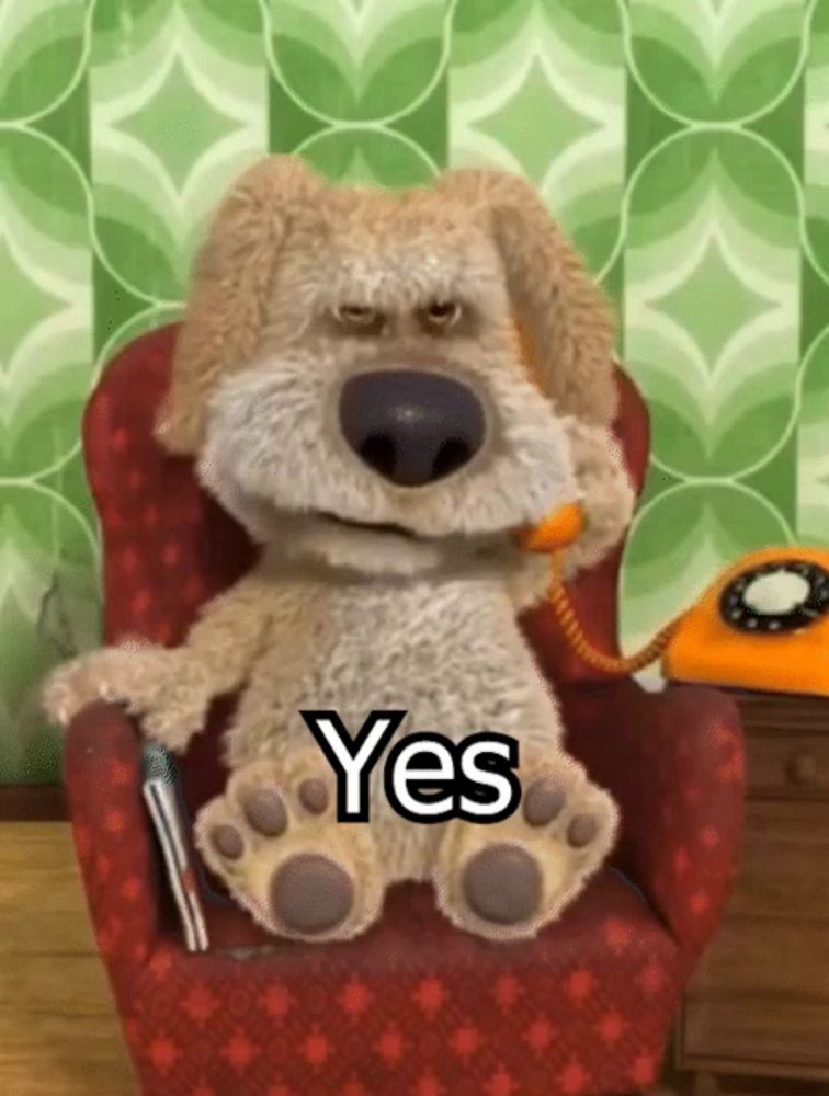 a stuffed dog is sitting in a chair with a phone in his mouth and says yes