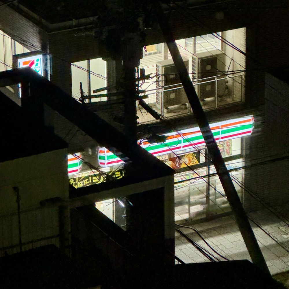 Night picture of a 7-Eleven store from above angle in the city of Nagasaki, Japan. The lights from the store luminate the dark street.