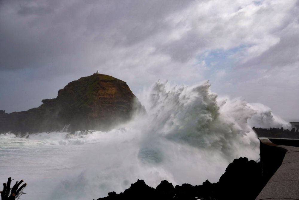 Storm waves crashing into the rocks along the promenade in Porto Moniz, Madeira. The sea is white with foaming water created by crashing over the rocks and smashed against the shoreline. The waves are coming high above the elevated promenade with dramatic effect.