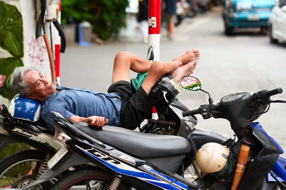 Man laying on his back on top a scooter in the streets of Hanoi Vietnam 