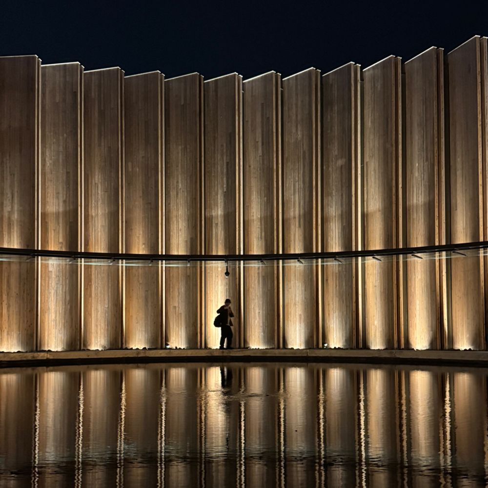 Central pond of the Japan Pavilion at Expo 2025 in Osaka. The round walls are illuminated and reflect on the pond. There is a sole person walking around the pond.
