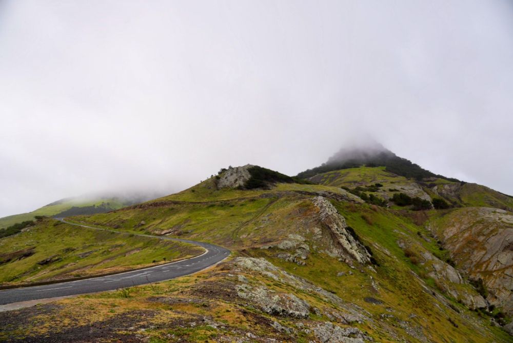 A road winds up a mountain with a cloud covering the peak