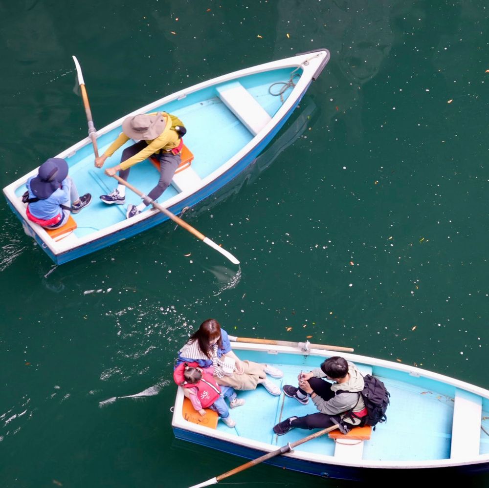 People boating in a gorge is southern Japan. The boats are light blue and the water deep green. The picture is taken from above the rowers.
