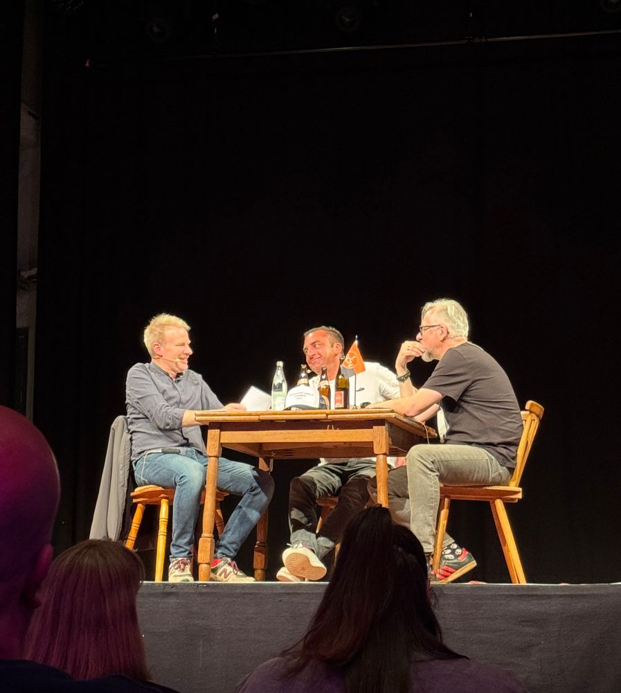 Die KaDepp-Podcaster Sebastian Gloser, Fadi Keblawi und Uli Digmayer (v.l.n.r.) an einem Tisch auf der Bühne im Nürnberger Z-Bau