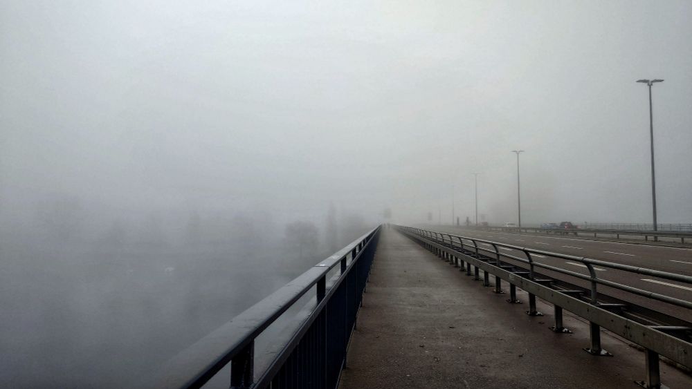 Blick auf den Radweg auf einer Brücke die im Nebel endet. Schemenhaft ist die andere Seite zu erkennen 