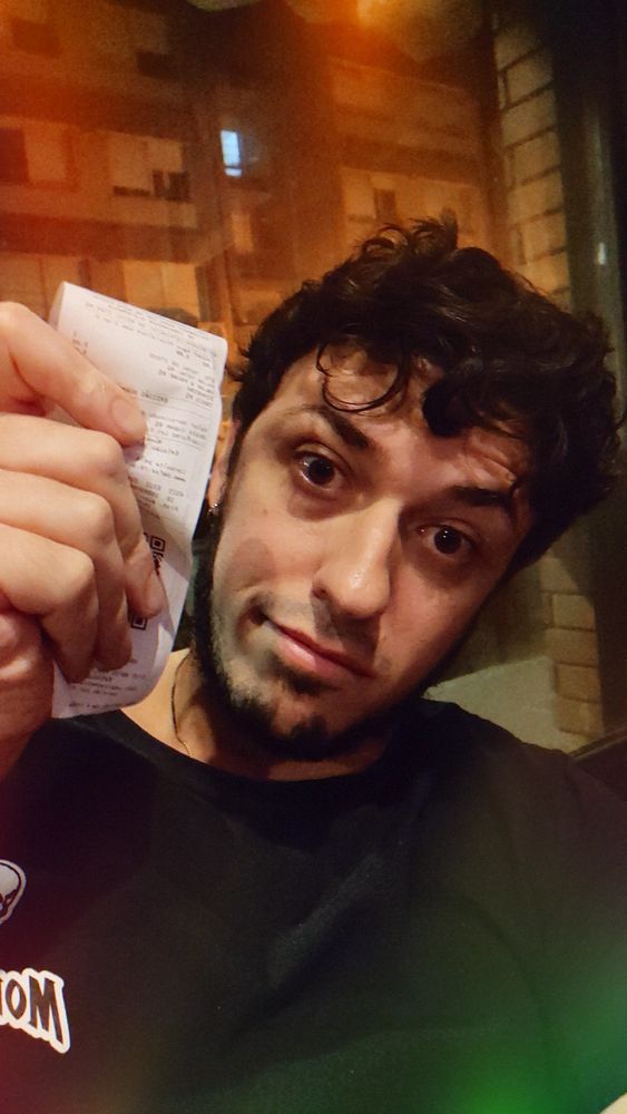 Uma bicha descabelada, acabada e visivelmente exausta (eu) segurando um pedaço de papel minúsculo e comprido que, aparentemente, é uma nota fiscal.