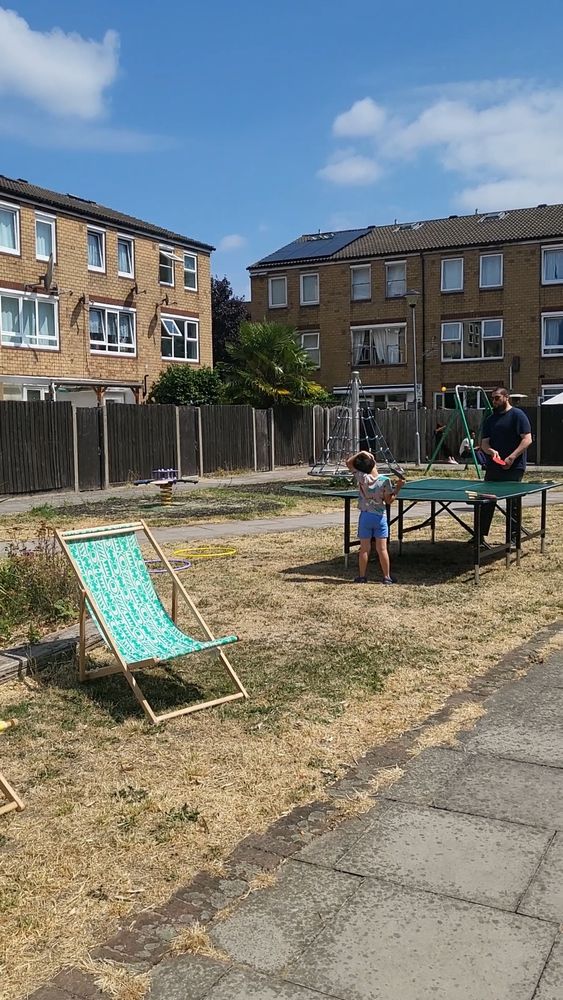 People playing table tennis, deck chair, houses in the background 