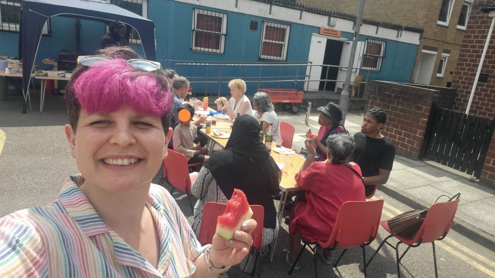 Zoë with a bit of watermelon in front of a table full of people outside a community hall