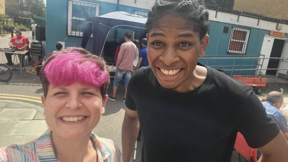 Zoë and Dylan smiling with community hall, DJ and BBQ behind 