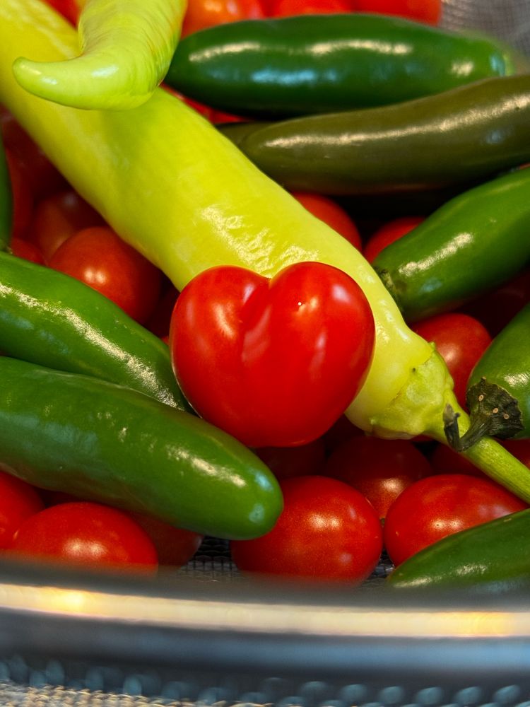 Dark green hot peppers, light yellow banana pepper and bright red cherry tomatoes, including a double cherry tomato in the shape of a heart. 