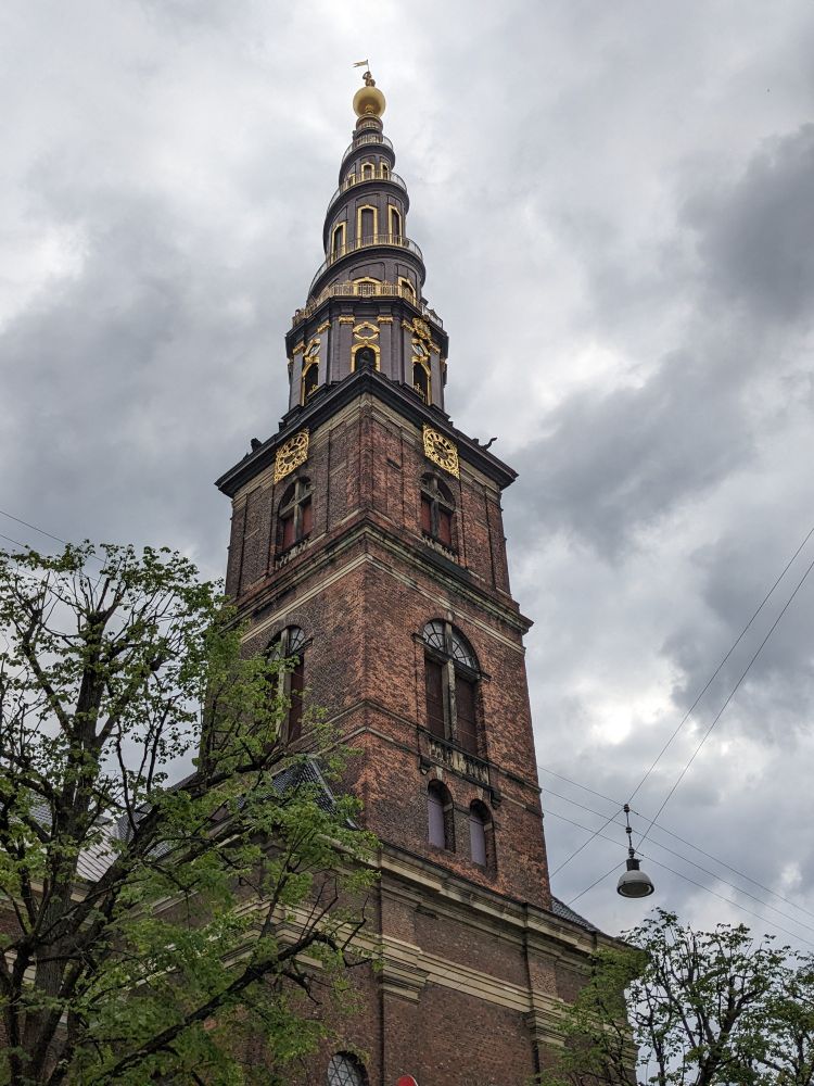 A view from street level of the Vor Frelsers Kirke, a Baroque Revival church in Copenhagen, Denmark, built with an exterior spiral staircase ascending its spire.